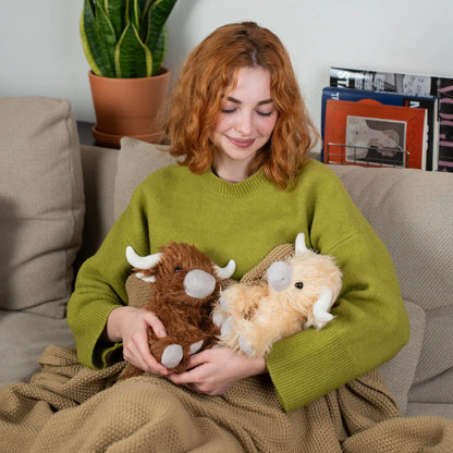 Woman sitting on a couch holding two plush toys, surrounded by a cozy living room setting.