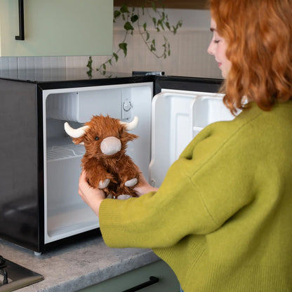 Person holding a stuffed animal cow in front of an open mini refrigerator.
