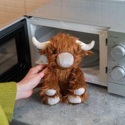 Heated plush toy Highland cow being held in front of a microwave oven.