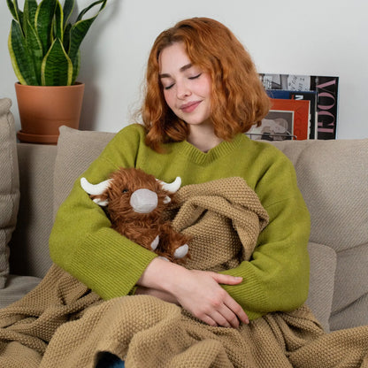Woman on couch cuddles weighed plush highland cow