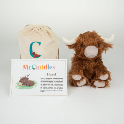 Plush toy Highland cow named Hazel with a drawstring bag and information card on a white background